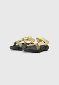 Sportsandalen met zwarte zolen, groene en gele banden, en verstelbare hardware voor een veilige pasvorm. Getextureerde voetbed voor grip.