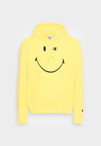 Sudadera con capucha amarilla hecha de algodón con un gran gráfico de cara sonriente negra en el frente. Incluye un bolsillo delantero y capucha con cordón.