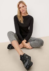 Schwarzer Strickpullover mit rundem Ausschnitt, kombiniert mit grauen gemusterten Jogginghosen und klobigen schwarzen und grauen Sneakers. Leger Outfit.