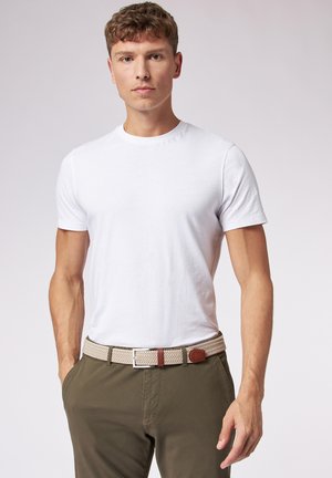 T-shirt di cotone bianco indossata con pantaloni verde oliva e una cintura intrecciata beige con accenti in pelle marrone. Inclusa una vista ravvicinata della fibbia della cintur