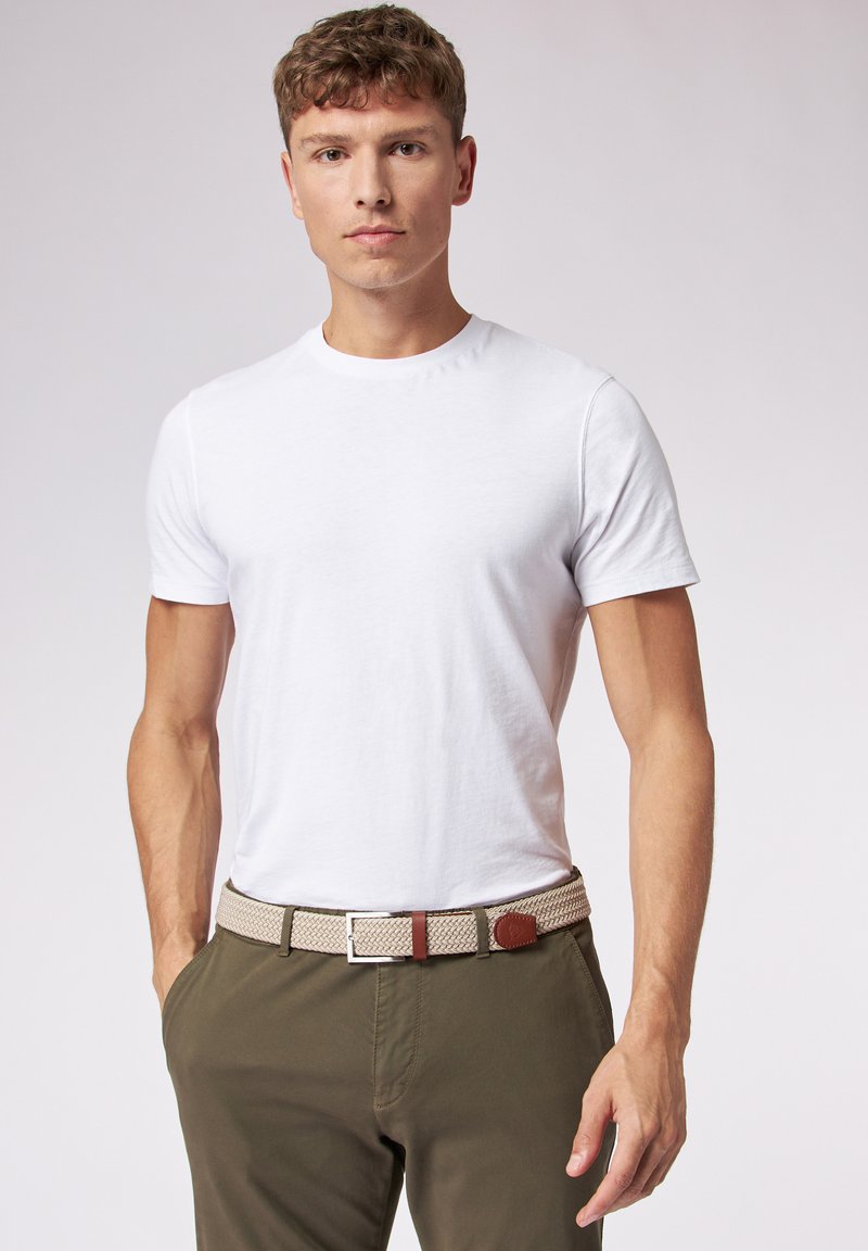 Witte katoenen t-shirt gedragen met olijfgroene broek en een geweven beige riem met bruine leren accenten. Close-up van de riembuckle inbegrepen.