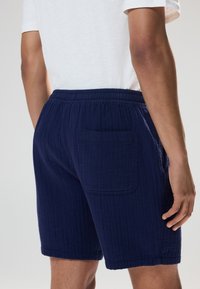 Marineblauwe korte broek van gestructureerde stof, met een elastische tailleband en een enkele achterzak. Lengte tot halverwege de dij.