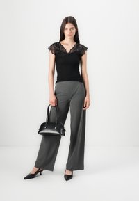 Top nero con maniche a cappuccio in pizzo, pantaloni grigi su misura e una piccola borsa nera. L'insieme presenta una silhouette aderente e un design a gamba affusolata.