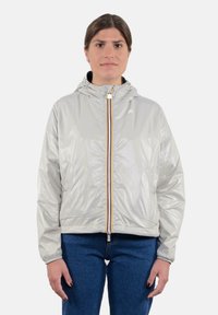 Giacca a vento leggera grigia chiara in materiale lucido, con zip frontale e dettagli arancioni e blu. Maniche a polsino e vestibilità rilassata.