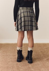 Plaid skirt in dark green and white with pleats, paired with black ankle boots and cream knitted socks. Textured background rug.