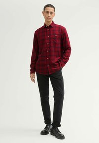 Czerwona i czarna koszula w kratę zapinana na guziki, z kieszenią na piersi, długimi rękawami i kołnierzykiem; w komplecie z czarnymi spodniami i skórzanymi butami.