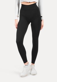 Hoge taille zwarte leggings van rekbare stof met een gladde textuur. Beschikt over een naadloze tailleband en een aansluitende silhoette voor comfort.