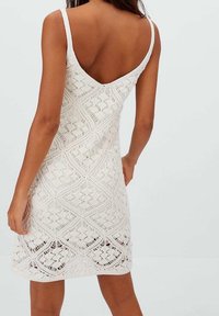 Robe blanche en crochet avec une coupe ajustée, des bretelles spaghetti et un dos en V profond. Le motif complexe présente des dessins géométriques sur toute la surface.