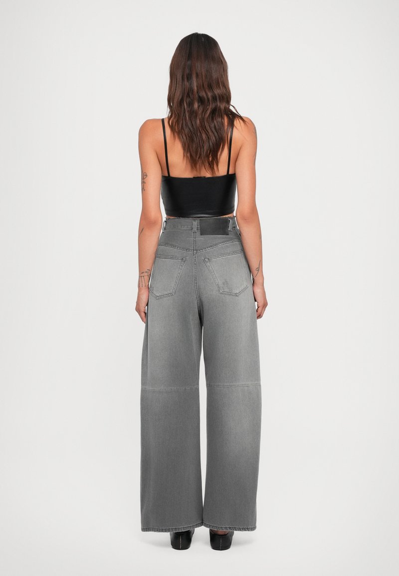 Breda grå denimbyxor med hög midja, utrustade med två bakfickor och en texturerad yta. Kombinerad med en svart linne.