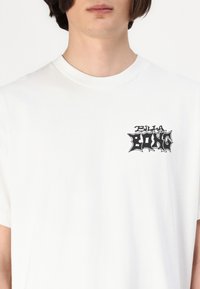 Hvid bomulds t-shirt med et sort grafisk logo på venstre brystområde. Korte ærmer og rund halsudskæring, glat tekstur.