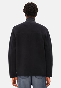 Schwarze Fleecejacke mit hohem Kragen, lockerer Passform und überschnittenen Schultern. Verfügt über eine glatte Textur und ein minimalistisches Design ohne sichtbare Beschläge.