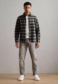 Black and green plaid flannel shirt, white crew neck t-shirt, distressed light grey jeans, and white sneakers against a neutral background.