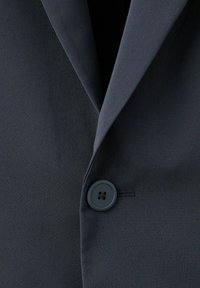 Temno modra suknjič z zarezenim ovratnikom in enim temnim gumbom, zaponjenim na sredini spredaj.