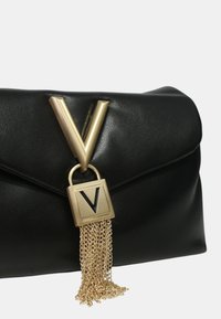 Clutch in pelle nera con chiusura a forma di V in oro, dotata di lucchetto quadrato e nappina a catena. Texture liscia con design minimalista.