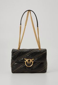 Černá kožená kabelka diagonálně prošitá, se zlatým řetízkem jako úchytem a dekorativními cvočky. Má zapínání ve tvaru zlatého ptáka.