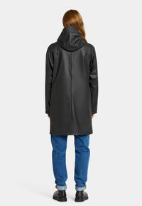 Svart vattentät regnjacka med huva, med en slät yta, knälång design och rak klippning. Matchad med blå denimbyxor.