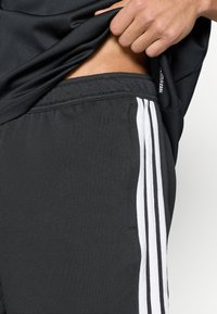 Μαύροι αθλητικοί σορτς από υφασμάτινη υφή, με λευκές ρίγες στα πλευρά και ελαστική μέση.