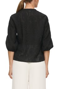 Blusa negra con estampado floral, con mangas abullonadas y cuello redondo, confeccionada en una tela ligera y transparente. El dobladillo es recto.