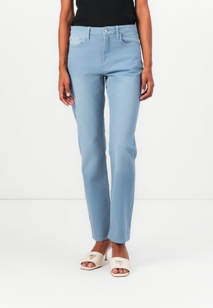 Light blue denim jeans with a slim fit, five-pocket design, and a button closure, paired with beige open-toe heels featuring a logo detail.