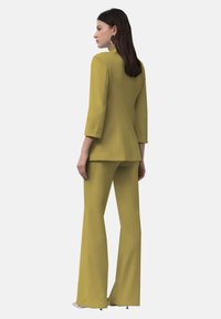 Blazer giallo su misura con maniche a tre quarti e pantaloni a palazzo coordinati, caratterizzati da una texture liscia e linee pulite.