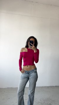 Top ajustado de manga larga y hombros al descubierto en un tejido de color rosa vibrante, combinado con unos jeans de lavado claro, ligeramente acampanados y con cintura.