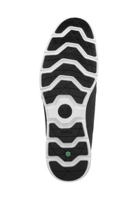 Black rubber shoe sole with a white midsole, featuring a patterned tread design and a green accent in the center. Tree logo on sole.