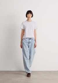 Hvit kortermet t-skjorte kombinert med lyseblå baggy jeans. Modellen har på seg brune sko. Den enkle bakgrunnen fremhever antrekket.