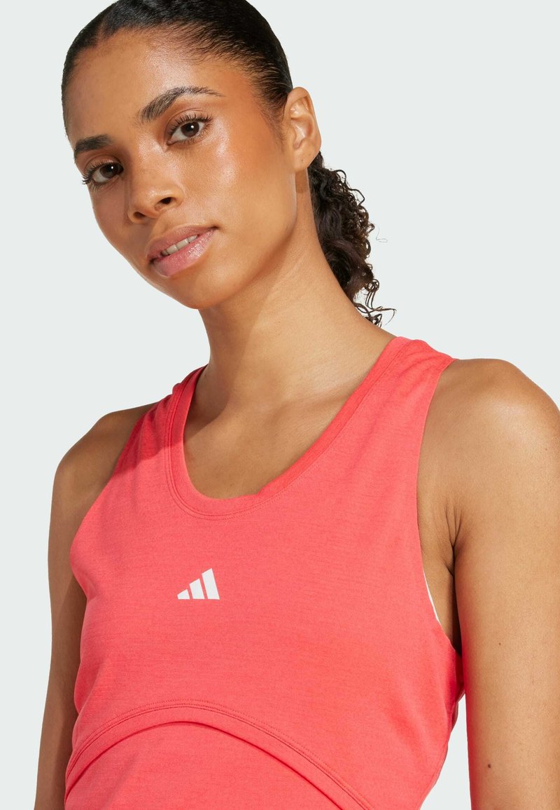 Débardeur de sport corail avec un col rond et un logo blanc. Le tissu semble léger avec une texture lisse. Gros plan sur l'épaule.