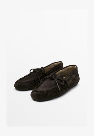 Ein Paar dunkelbraune Wildleder-Mokassins mit runden Zehen und gebundenen Schleifenbändern auf einem weißen Hintergrund.