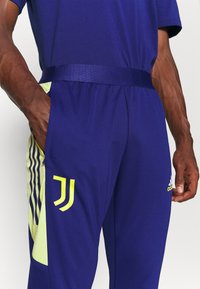 Fioletowe spodnie sportowe z teksturowanej tkaniny, z żółtymi akcentami, wzorzystym bocznym panelem i elastycznym paskiem w talii.