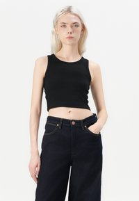 Čierny rebrovaný crop top s okrúhlym výstrihom, doplnený o tmavé džínsy s vysokým pásom, ktoré majú viditeľné švy a zapínanie na gombík.