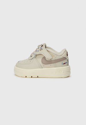 Nike Air Force 1 sneakers in sandy beige leather with pastel accents, textured sole, unique lacing, and a subtle brand logo on the heel.