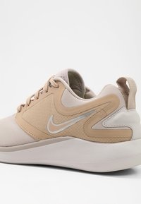 Beige sportskor med texturerad ovandel, släta detaljer, reflekterande logotyp och en dämpad, formad sula.