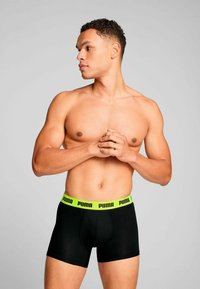 Black boxer briefs with a green PUMA logo waistband, fitted design, smooth fabric, and snug shape displayed on a male figure.