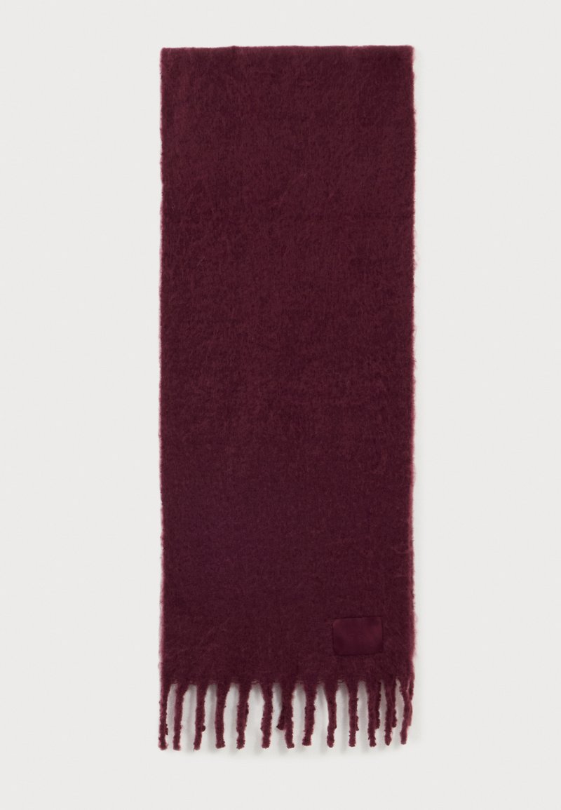 Écharpe duveteuse rouge foncé avec franges torsadées à une extrémité et une petite pièce de tissu près des franges.