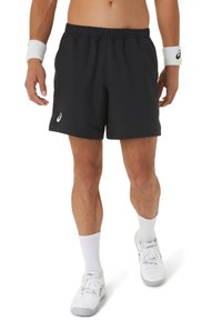 Schwarze Sportshorts mit elastischem Bund, aus leichtem Material, mit einem weißen Logo auf der linken Seite. Getragen mit weißen Accessoires.