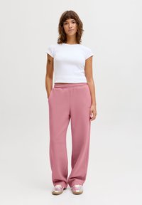 Světle růžové tepláky mají volný střih s elastickým pasem a postranními kapsami, doplněné o přiléhavý bílý top s krátkými rukávy.