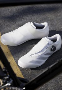 Scarpe da ciclismo bianche con superiore testurizzato, design minimalista, punta liscia e sistema di chiusura con rotella laterale.