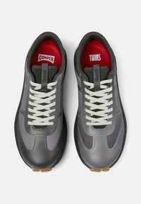 Grijze sneakers met contrasterende panelen, voorzien van witte veters en een rode binnenzool met het label "CAMPER" en "TWINS." Unieke designelementen zichtbaar.