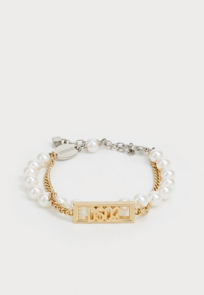 Bracelet doré mettant en vedette un charme rectangulaire avec "DS02", combiné avec des perles en nacre blanche et un élément de chaîne en or torsadé.