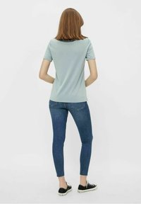 Camiseta de manga corta azul claro combinada con jeans ajustados azul oscuro y zapatillas negras, vista desde la parte de atrás. Tela suave, diseño ceñido.