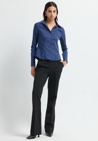 Camicia blu navy a maniche lunghe con bottoni, decorata con strisce verticali bianche, dotata di colletto a punta e design aderente, abbinata a pantaloni neri.