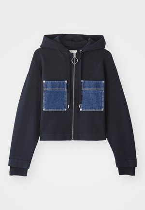 Marineblauwe cropped sweatshirt met een rits aan de voorkant, grote denimpocketzakken en een trekkoordcapuchon. Kenmerkt geribbelde manchetten en een zilveren ringtrekker.
