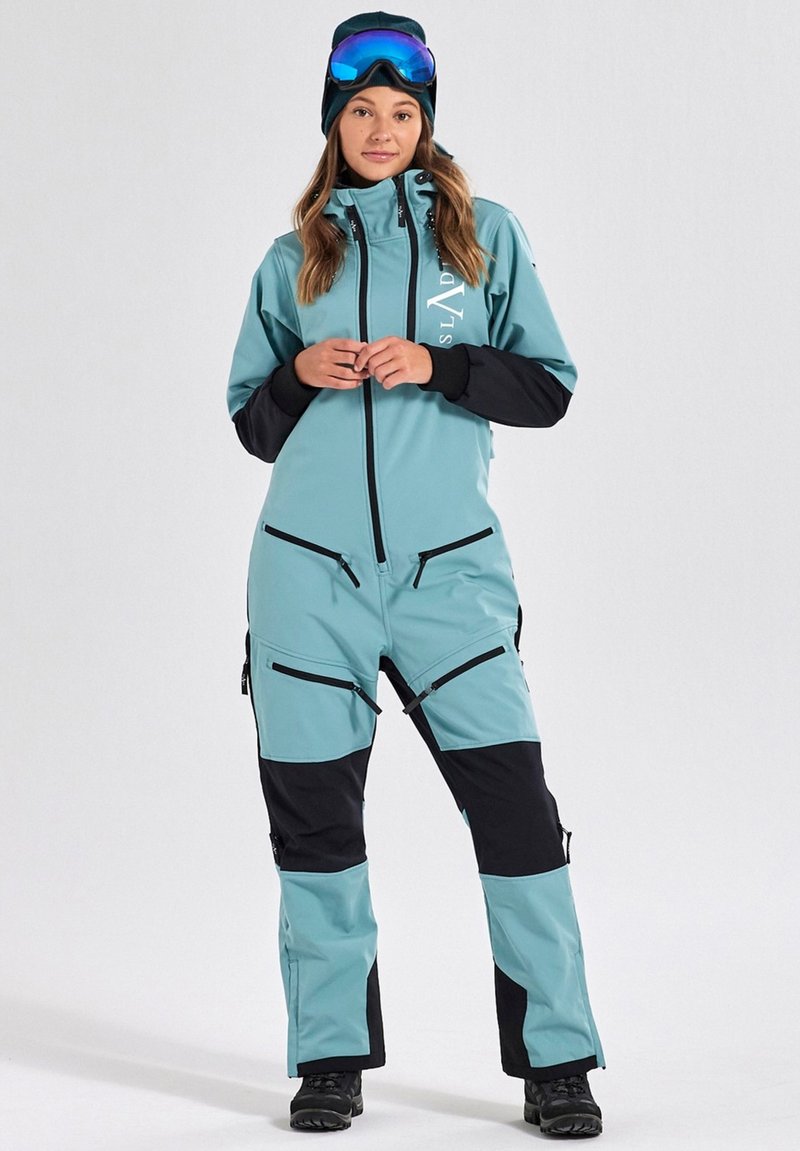 Teal ski suit with black accents, zippered pockets, and fitted design. Includes a high collar and integrated hood, made from durable fabric.