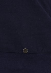 Tessuto di cotone blu navy con una texture liscia, caratterizzato da un accento metallico rotondo con testo inciso nella parte inferiore. Design semplice e minimalista.