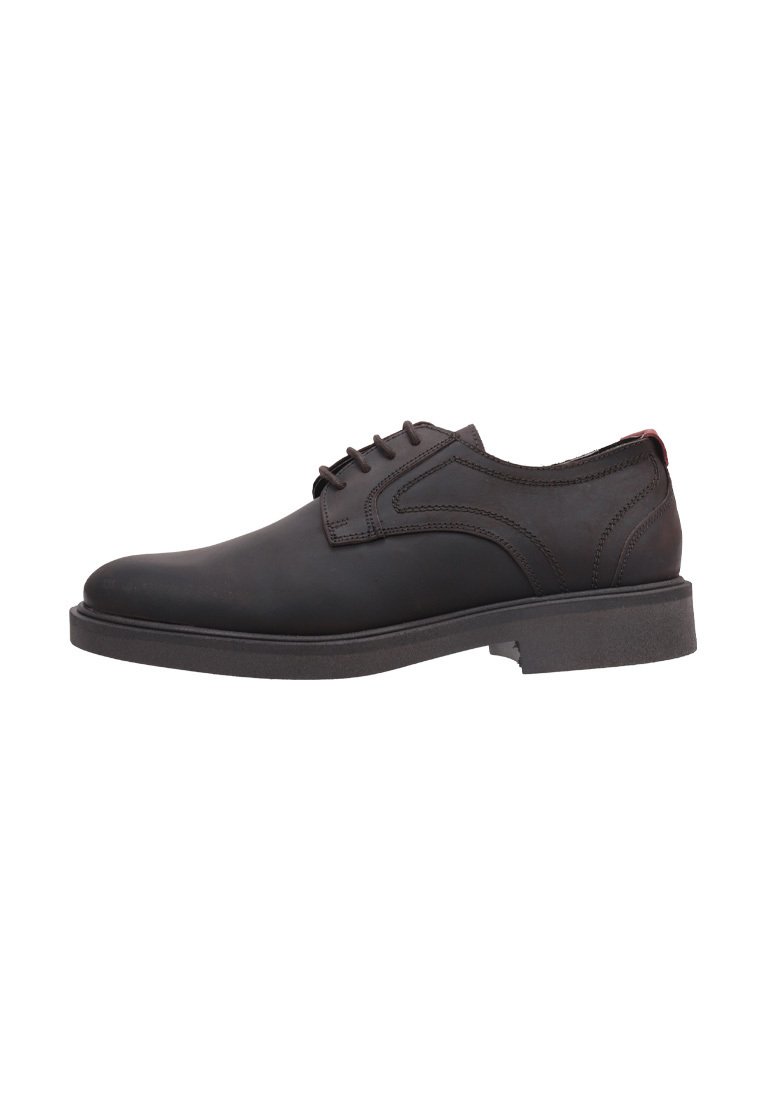 Zapato de vestir de cuero negro con punta redonda, diseño de cordones, costuras detalladas y suela gruesa de goma. Acentuado por una etiqueta roja en el talón.