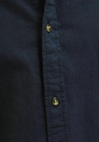 Marineblauwe knoop shirt met een textuur van linnen, voorzien van een zichtbare knoop en een net gestikte paspel.
