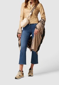 Beige leren jas, blauwe wijde spijkerbroek, patroonige sjaal, crème crossbodytas en beige sneakers met zwarte accenten. Decoratieve franjes aan de sjaal.