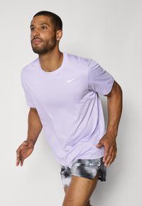 Light purple Nike t-shirt with a round neckline and short sleeves, paired with gray patterned shorts featuring a logo on the hem.