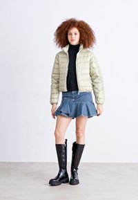 Lettgrønn jakke med puffer, svart genser med høy hals, denim skjørt med utsvingte ben, og knelange svarte støvler med brede såler. Enkel og moderne design.